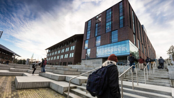 student walking up steps to discovery hall with a blue sky and clouds behind it