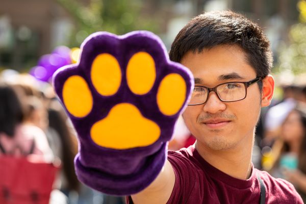 A person wearing glasses holding a purple and yellow paw print.