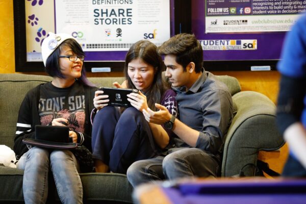 A group of people sitting on a couch looking at a device.