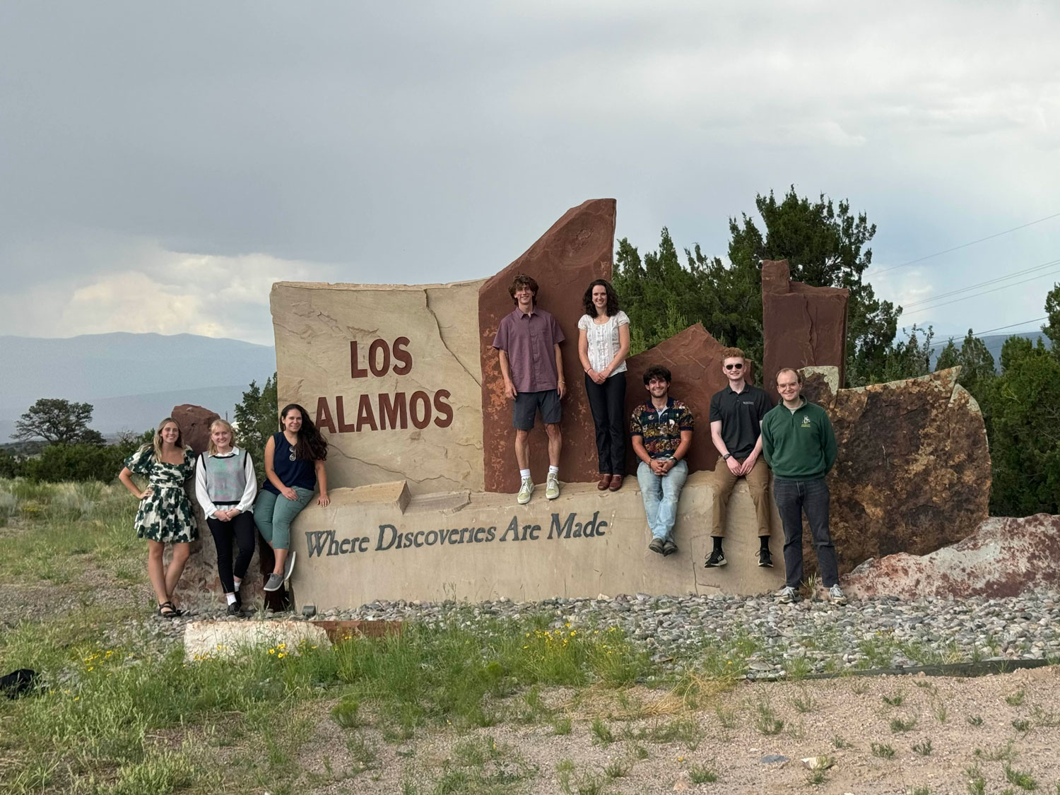 A group of people at a sign that reads "Los Alamos, where discoveries are made."