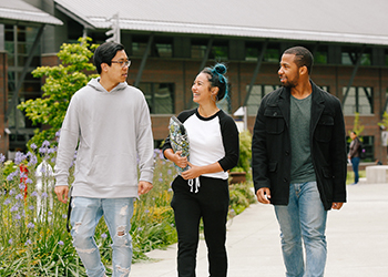 Three people smiling and walking down a pathway on campus.