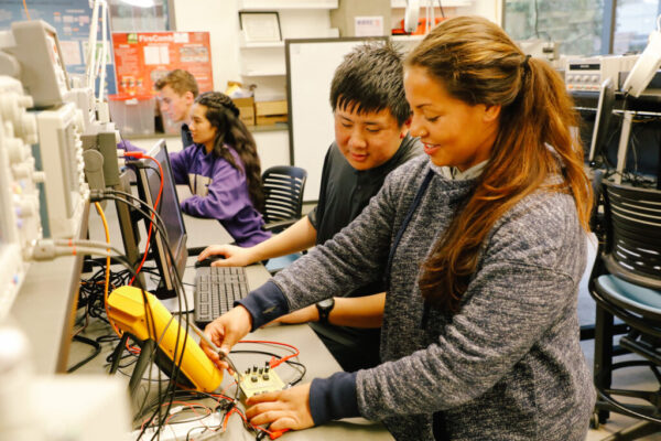 Two students testing electrical charge on amplifier. 