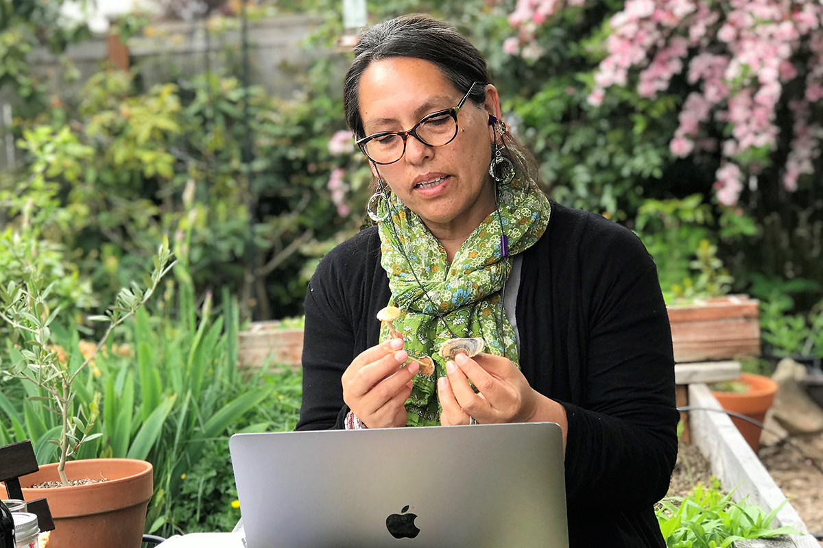 Ursula in front of her laptop holding up some plant life